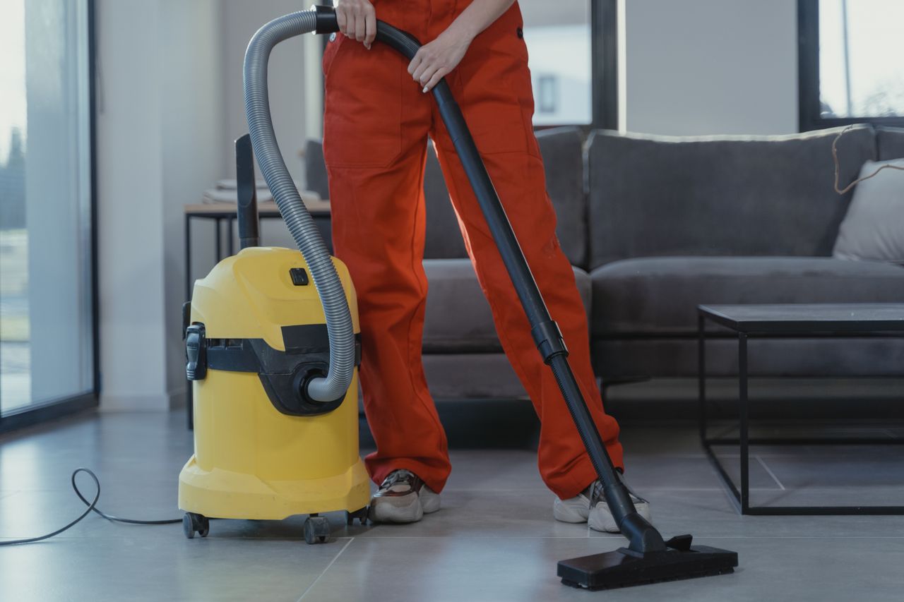 project-01-d A professional cleaner in red coveralls vacuums a contemporary living room with a yellow vacuum cleaner.